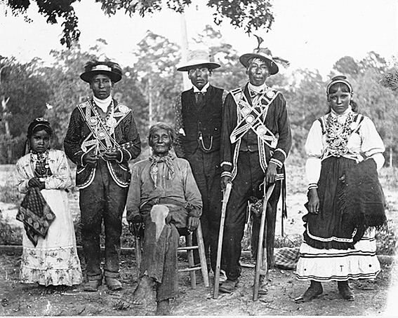 Group of Choctaw men, a young woman and a young girl posed outdoors, probably at a stick ball game, Neshoba County and Scott County, Mississippi, 1908. Photograph by Mark Raymond Harrington. Courtesy of the National Museum of the American Indian, Mississippi Choctaw Collection, N02667.