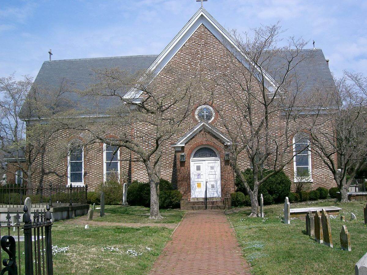Photograph of the south side of St. John's Episcopal Church, an old brick building with weathered gravestones in the front yard.