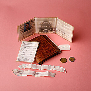 Photograph of a wallet, ID card, coins, and papers displayed on a pink background.
