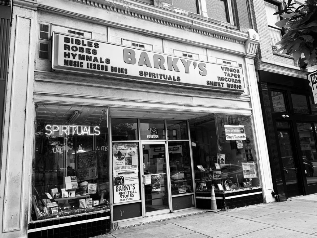 Black and white photograph of the storefront of Barky's Record Shop advertising Bibles, robes, hymnals, spirituals, videos, tapes, records, sheet music, and other items.
